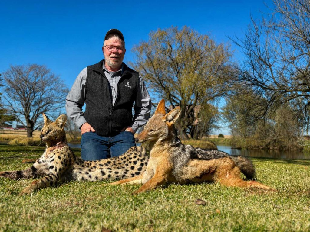 Hunter posing with a serval and black-backed jackal during an African hunting safari in South Africa.