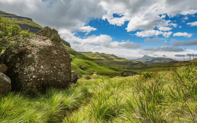 Mountainous Southern African landscape with rocky outcrops, open grassland and dramatic clouds.