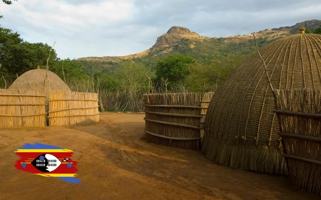 Traditional Swazi homestead with thatched huts and mountain scenery in Eswatini.